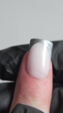 Moda tarzında Fransız manikürü: gümüş ve sütlü jel hassas geometri ve makro odaklı rafine form. Tırnak teknisyeninin siyah eldiveni derinlik katıyor ve tasarımın inceliğini vurguluyor..