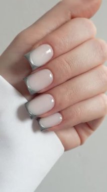 Siyah eldivenli profesyonel manikürcü müşterileri gümüş Fransız manikürcüsüyle tutuyor. Beyaz arkaplan, temiz ve minimal stil. Profesyonel tırnak işçiliğinin hassasiyeti ve özeni vurgulanıyor. Ders ve güzellik eğitimi içeriği için mükemmel