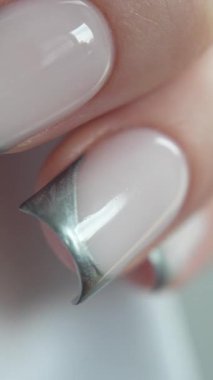 Siyah eldivenli profesyonel manikürcü müşterileri gümüş Fransız manikürcüsüyle tutuyor. Beyaz arkaplan, temiz ve minimal stil. Profesyonel tırnak işçiliğinin hassasiyeti ve özeni vurgulanıyor. Ders ve güzellik eğitimi içeriği için mükemmel