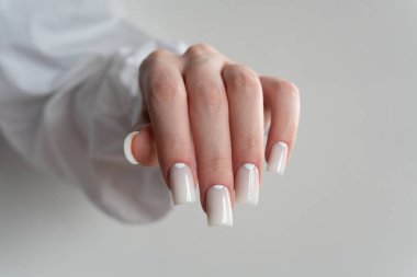 Zarif beyaz tırnaklar, parlak manikür, düzgün kare şekilli, yumuşak estetik. Arka plan hafifçe bulanık, nazik ve estetik bir görünüm yaratıyor..