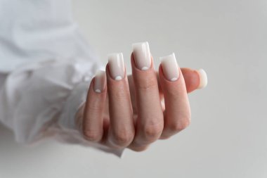 Temiz beyaz manikür, parlak uzun tırnaklar, güzellik salonu ayrıntıları, en az kadınsı tarz. Beyaz, uzun kollu bir elbise giyiyor. Minimalist ve zarif bir tarzı var..