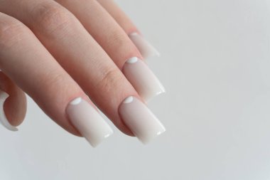 Pürüzsüz beyaz tırnaklar zarif manikür, parlak bir son, yakın çekim moda güzellik çekimi. Parmaklar nazikçe kıvrılmış ve yumuşak ışıklandırma çivilerin parlak görünümünü arttırıyor. 