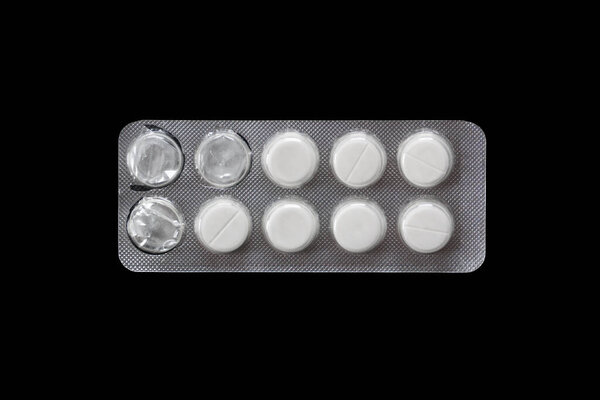 White round tablets in blister pack. Close-up macro of medical pills for pain relief, antibiotics, or vitamins, isolated on dark background.