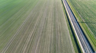 Geniş yeşil tarımsal alanlarda akan demiryolu raylarını vurgulayan bir hava manzarası, kırsal manzaraların uyumunu ve sakin bir ortamda ulaşım altyapısını yakalıyor.