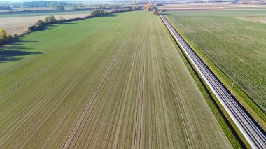 An aerial photograph showing railway lines extending across vast green fields, highlighting the intersection of agriculture and modern infrastructure in a serene rural landscape. clipart