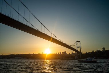 İstanbul Boğazı Köprüsü 'nün gün batımında nefes kesen manzarası, köprünün silueti gökyüzünün canlı renklerine karşı, aşağıdaki sakin sulara yansıyor..