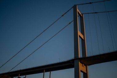 A breathtaking view of the Istanbul Bosphorus Bridge at sunset, with the bridge silhouetted against the vibrant colors of the sky, reflecting on the calm waters below. clipart