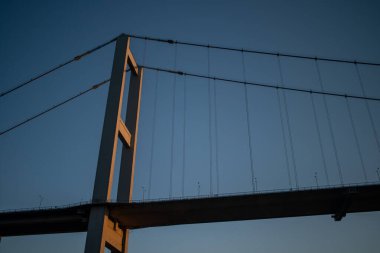 İstanbul Boğazı Köprüsü 'nün gün batımında nefes kesen manzarası, köprünün silueti gökyüzünün canlı renklerine karşı, aşağıdaki sakin sulara yansıyor..