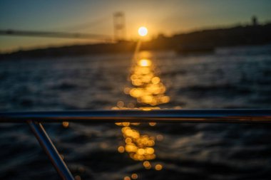 Batan güneşin altın rengi, köprüye ve sakin sulara sıcak bir parıltı saçar, sahnenin zarafetini yakalar..