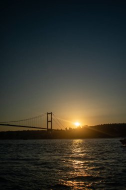 Batan güneşin altın rengi, köprüye ve sakin sulara sıcak bir parıltı saçar, sahnenin zarafetini yakalar..