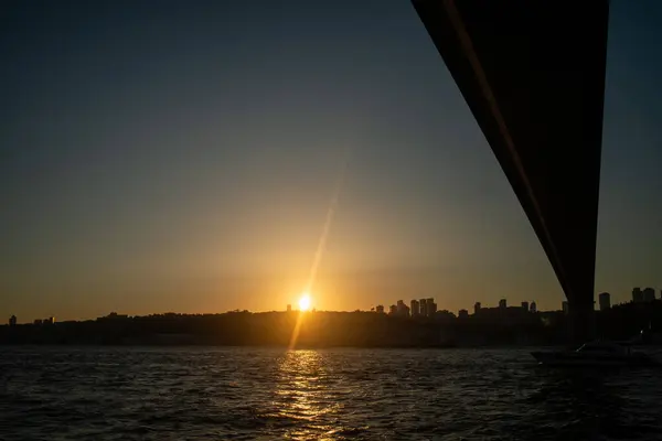 İstanbul Boğazı Köprüsü 'nün gün batımında nefes kesen manzarası, köprünün silueti gökyüzünün canlı renklerine karşı, aşağıdaki sakin sulara yansıyor..
