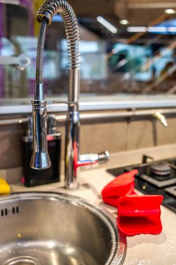 Musluktan akan musluk suyuyla dolu bir mutfak sahnesinde, canlı kırmızı yemek eldivenleriyle birlikte, yemek hazırlamada hem işlevsellik hem de stili vurgulanıyor..