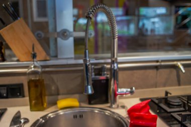 Musluktan akan musluk suyuyla dolu bir mutfak sahnesinde, canlı kırmızı yemek eldivenleriyle birlikte, yemek hazırlamada hem işlevsellik hem de stili vurgulanıyor..