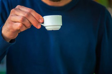 Mavi gömlekli bir adamın beyaz bir fincanda servis edilen geleneksel Türk kahvesinin keyfini çıkarırken çekilmiş bir fotoğraf çok hoş bir kültürel an sergiliyor..