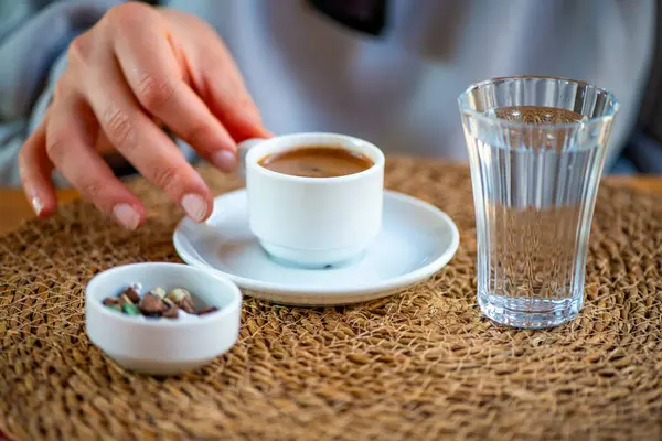 Geleneksel Türk kahvesini bir bardak su ve çakıl taşı çikolatasıyla içen bir kadının fotoğrafı, harika bir kültürel sunum sergiliyor..