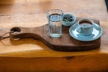 Çakıl taşlı çikolata ve bir bardak suyla Türk kahvesi sunumu, masada geleneksel ve zarif bir düzenleme sergileniyor.