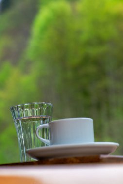 Çakıl taşlı çikolata ve bir bardak suyla Türk kahvesi sunumu, doğada yemyeşil bir yaprak zeminine karşı hazırlanıyor.