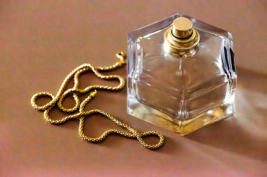 Bir şişe parfümün yanında zarifçe sarılı altın bir kolyenin yer aldığı lüks bir sahne..