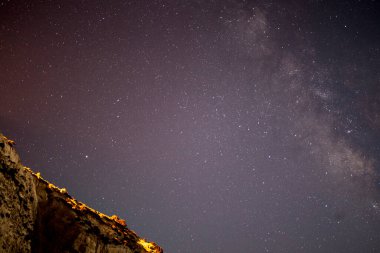 Samanyolu 'nun deniz ve dağ üzerindeki gece gökyüzünü süslediği nefes kesici bir kıyı manzarası dingin ve kozmik bir mucize yaratıyor..