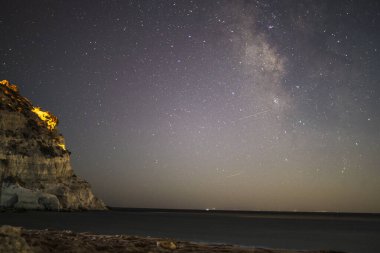 Samanyolu 'nun deniz ve dağ üzerindeki gece gökyüzünü süslediği nefes kesici bir kıyı manzarası dingin ve kozmik bir mucize yaratıyor..