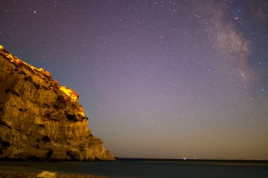 Samanyolu 'nun deniz ve dağ üzerindeki gece gökyüzünü süslediği nefes kesici bir kıyı manzarası dingin ve kozmik bir mucize yaratıyor..