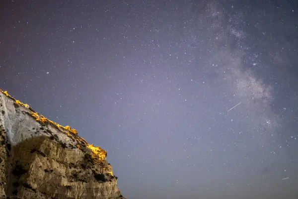 Samanyolu 'nun deniz ve dağ üzerindeki gece gökyüzünü süslediği nefes kesici bir kıyı manzarası dingin ve kozmik bir mucize yaratıyor..