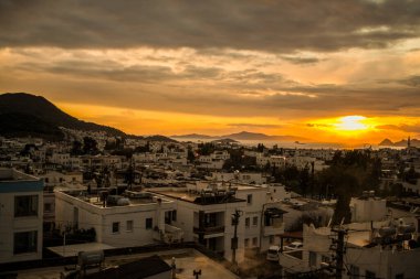 Türkiye 'nin Bodrum kentindeki sahil kasabasında güzel bir günbatımı, akşam gökyüzünü canlı renklerle boyar, dingin ve pitoresk bir deniz manzarası yaratır.