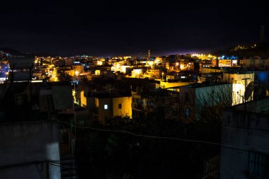 Şehir ışıklarının parlayan gökyüzü ve atmosferik gece titreşimleriyle canlı bir şehir manzarası yarattığı büyüleyici bir gece manzarası.