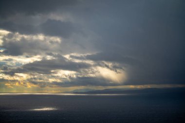 Bulutların ve güneş ışınlarının denize yansıdığı sakin bir sahne, doğanın güzelliğini ve suyun üzerindeki güneş ışığının etkileşimini sakin ve nefes kesici bir şekilde gösteriyor.