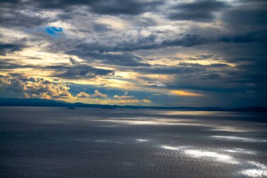 Bulutların ve güneş ışınlarının denize yansıdığı sakin bir sahne, doğanın güzelliğini ve suyun üzerindeki güneş ışığının etkileşimini sakin ve nefes kesici bir şekilde gösteriyor.