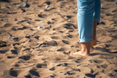 Doğayla olan huzurlu bağlantıyı hisset. Bir kadın kumların üzerinde yalınayak yürüyor, ayaklarının altındaki dünyayı kucaklıyor..