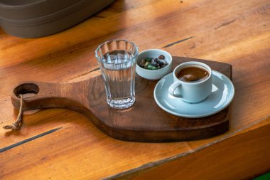 Çakıl taşlı çikolata ve bir bardak suyla Türk kahvesi sunumu, masada geleneksel ve zarif bir düzenleme sergileniyor.