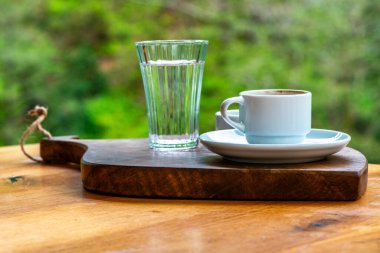 Turkish coffee presentation with pebble chocolate and a glass of water, set against a backdrop of lush foliage in nature. clipart