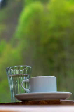 Çakıl taşlı çikolata ve bir bardak suyla Türk kahvesi sunumu, doğada yemyeşil bir yaprak zeminine karşı hazırlanıyor.