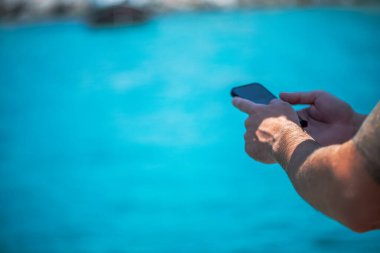 Uçsuz bucaksız mavi denizin arka planında cep telefonu tutan bir insan modern teknolojiyi okyanus yolculuğunun sükunetiyle harmanlıyor..