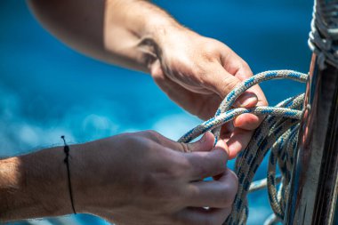Yelkenli ipiyle güçlü bir düğüm atan, denizcilik zanaatkarlığı ve yelkencilik uzmanlığı sergileyen ellerin yakın çekimi..