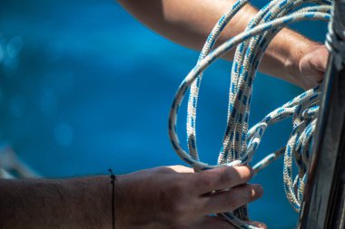 Yelkenli ipiyle güçlü bir düğüm atan, denizcilik zanaatkarlığı ve yelkencilik uzmanlığı sergileyen ellerin yakın çekimi..