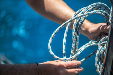 Yelkenli ipiyle güçlü bir düğüm atan, denizcilik zanaatkarlığı ve yelkencilik uzmanlığı sergileyen ellerin yakın çekimi..