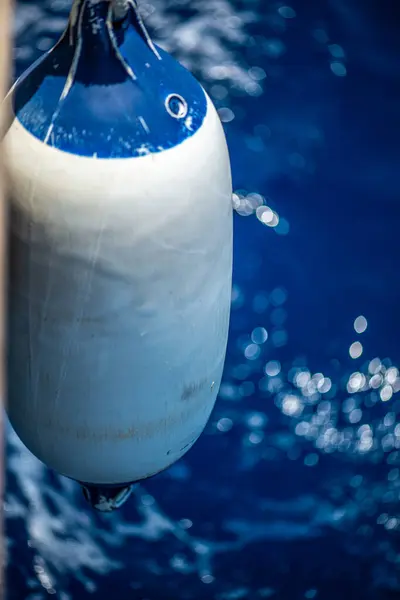 Bir yelkenliye bağlı çamurluğun detaylı bir yakın çekimi okyanus dalgaları etrafında ritmik bir hareket oluştururken hafifçe suya dokunuyor..