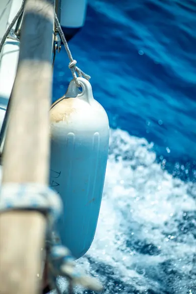 Bir yelkenliye bağlı çamurluğun detaylı bir yakın çekimi okyanus dalgaları etrafında ritmik bir hareket oluştururken hafifçe suya dokunuyor..