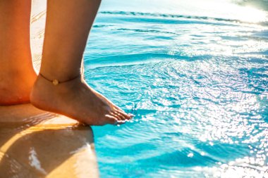 Bir kadının, batan güneşin sıcacık parıltısıyla aydınlanan bacağıyla havuz suyunu neşeyle sıçrattığı rüya gibi ve ferahlatıcı bir an..