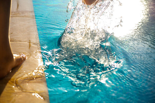 Мечтательный и освежающий момент, когда женщина игриво брызгает водой из бассейна своей ногой, освещенной теплым сиянием заходящего солнца.