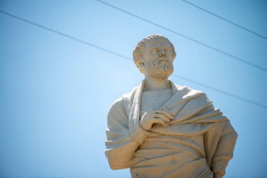 Filozofların bilge ifadelerini ve yaşlanmış taşın karmaşık dokularını vurgulayan bir Aristo heykelinin detaylı bir yakın çekimi.