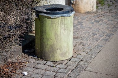 Şehir sokağının kenarına konmuş standart bir çöp kutusunun olduğu gerçekçi bir sokak sahnesi..