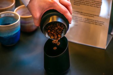 Bir kadının seramik fincana zengin, koyu kahve çekirdekleri koyduğu hassas anı gösteren yakın çekim, doğal bir ışık fotoğrafı..