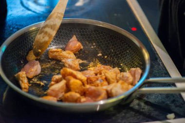 Yakın çekim, yüksek detay makro çekim. Bir kadın tavuk sotesi hazırlarken, cızırtılı malzemeler sergilerken ve sıcak bir mutfak ortamında yemek pişirirken görülüyor.