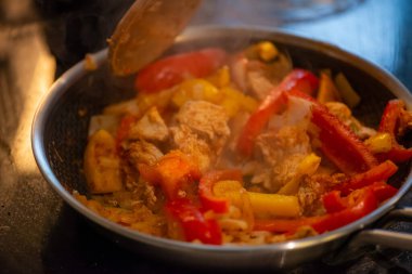 Yakın çekim, yüksek detay makro çekim. Bir kadın tavuk sotesi hazırlarken, cızırtılı malzemeler sergilerken ve sıcak bir mutfak ortamında yemek pişirirken görülüyor.