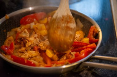 Yakın çekim, yüksek detay makro çekim. Bir kadın tavuk sotesi hazırlarken, cızırtılı malzemeler sergilerken ve sıcak bir mutfak ortamında yemek pişirirken görülüyor.