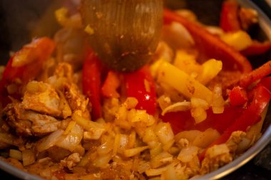 Yakın çekim, yüksek detay makro çekim. Bir kadın tavuk sotesi hazırlarken, cızırtılı malzemeler sergilerken ve sıcak bir mutfak ortamında yemek pişirirken görülüyor.