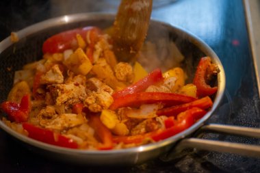 Yakın çekim, yüksek detay makro çekim. Bir kadın tavuk sotesi hazırlarken, cızırtılı malzemeler sergilerken ve sıcak bir mutfak ortamında yemek pişirirken görülüyor.